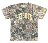A camouflage short-sleeve t-shirt with 'HEIGHTS' printed vertically in beige on the front, laid flat on a dark gray floor.